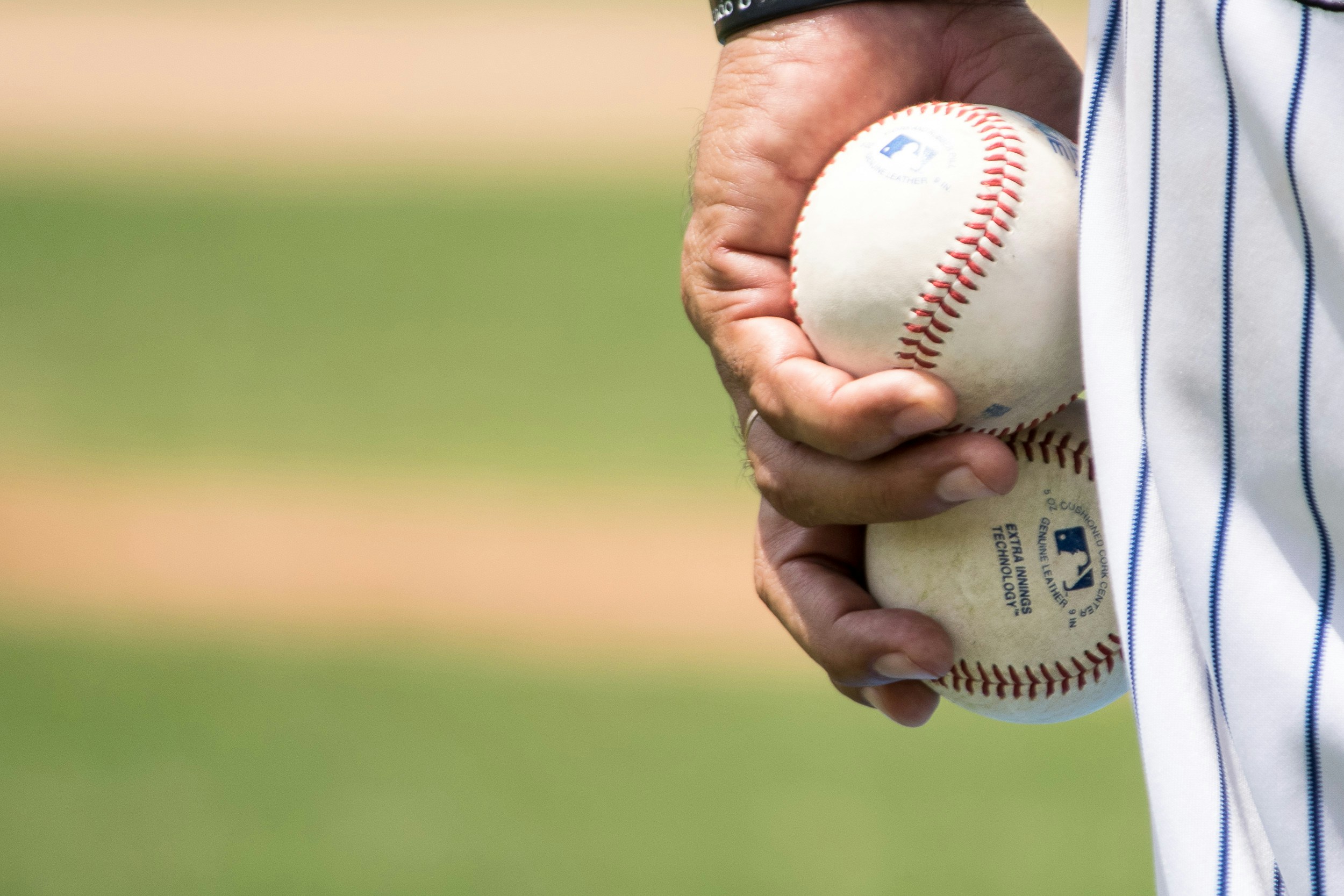 A player's hand holding two baseballs.